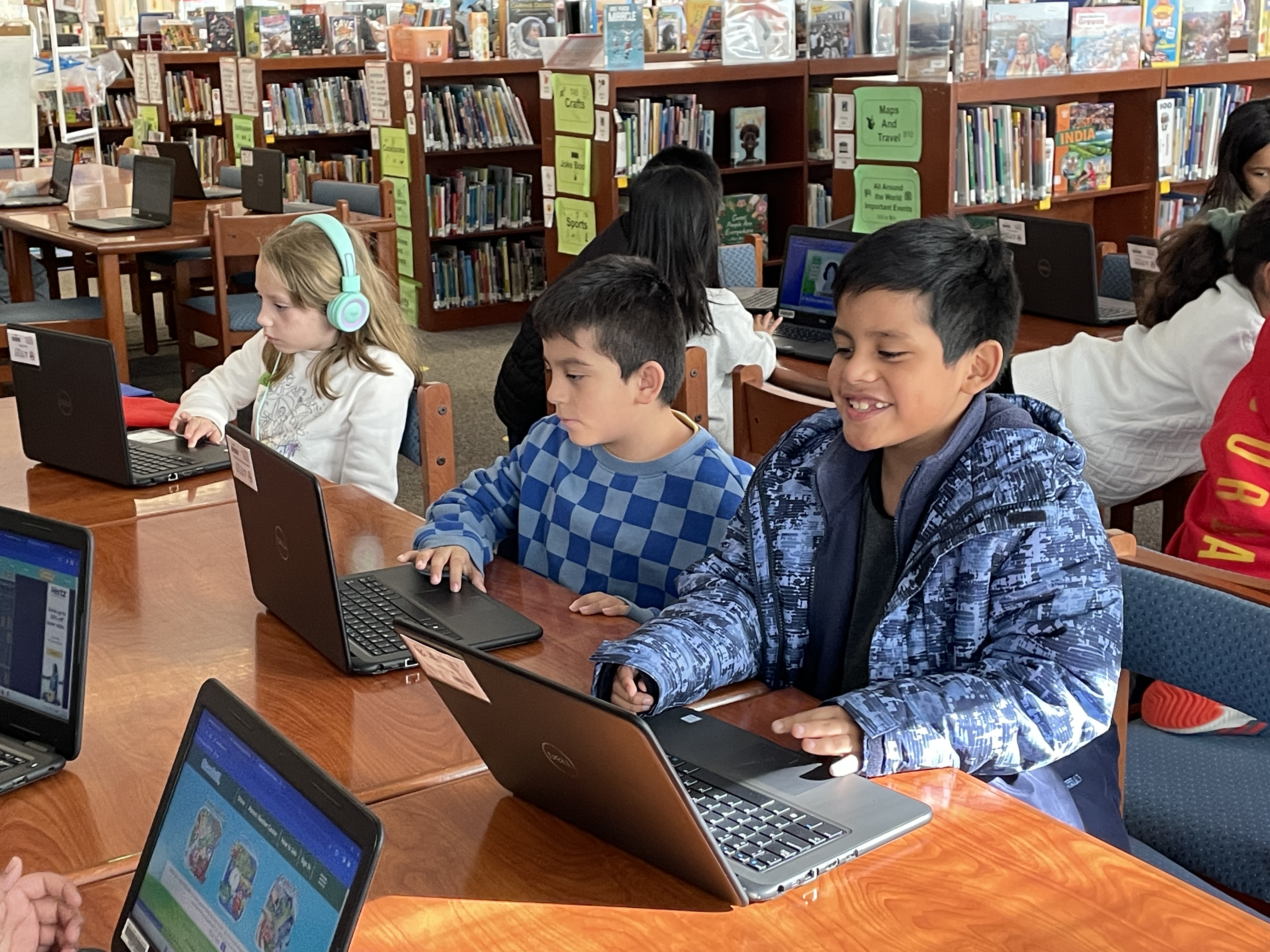 Students smile while using computers in the library during tech time
