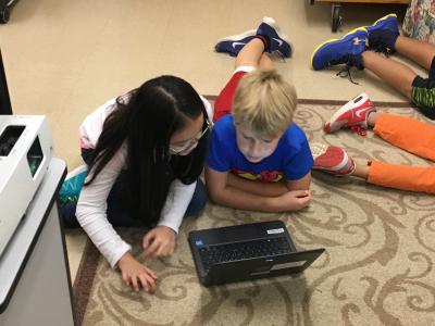 A boy and girl sharing a laptop while lying on the floor