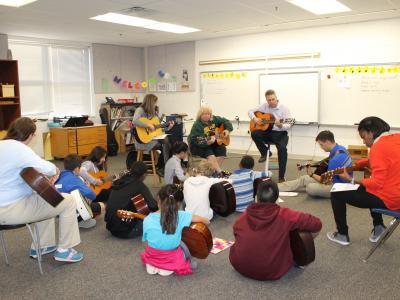 students on the floor and staff on chairs playing guitar