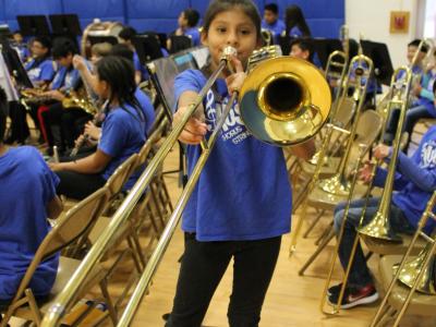 A girl stands and plays a trombone as tall as she is!