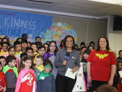 Anchor and Anna Woodward in front of a crowd of super hero students