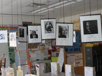 Biographical pamphlets line desks while photos hang from ceiling tiles (view 1)