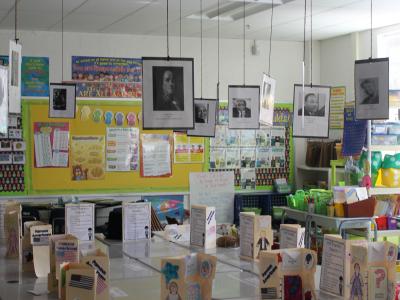Biographical pamphlets line desks while photos hang from ceiling tiles (view 2)