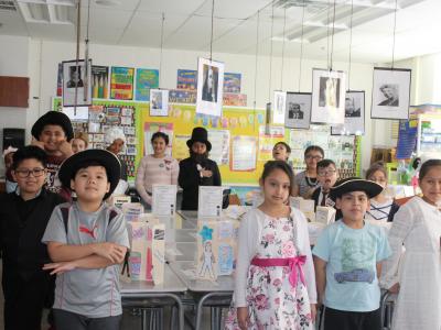 Students stand around desks in biographical costumes