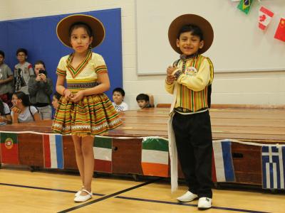 A young boy and girl in tan hispanic clothing dance